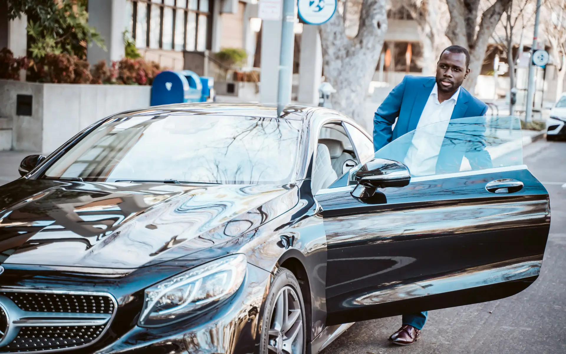 Executive in a suit stepping out of a black Mercedes-Benz sedan