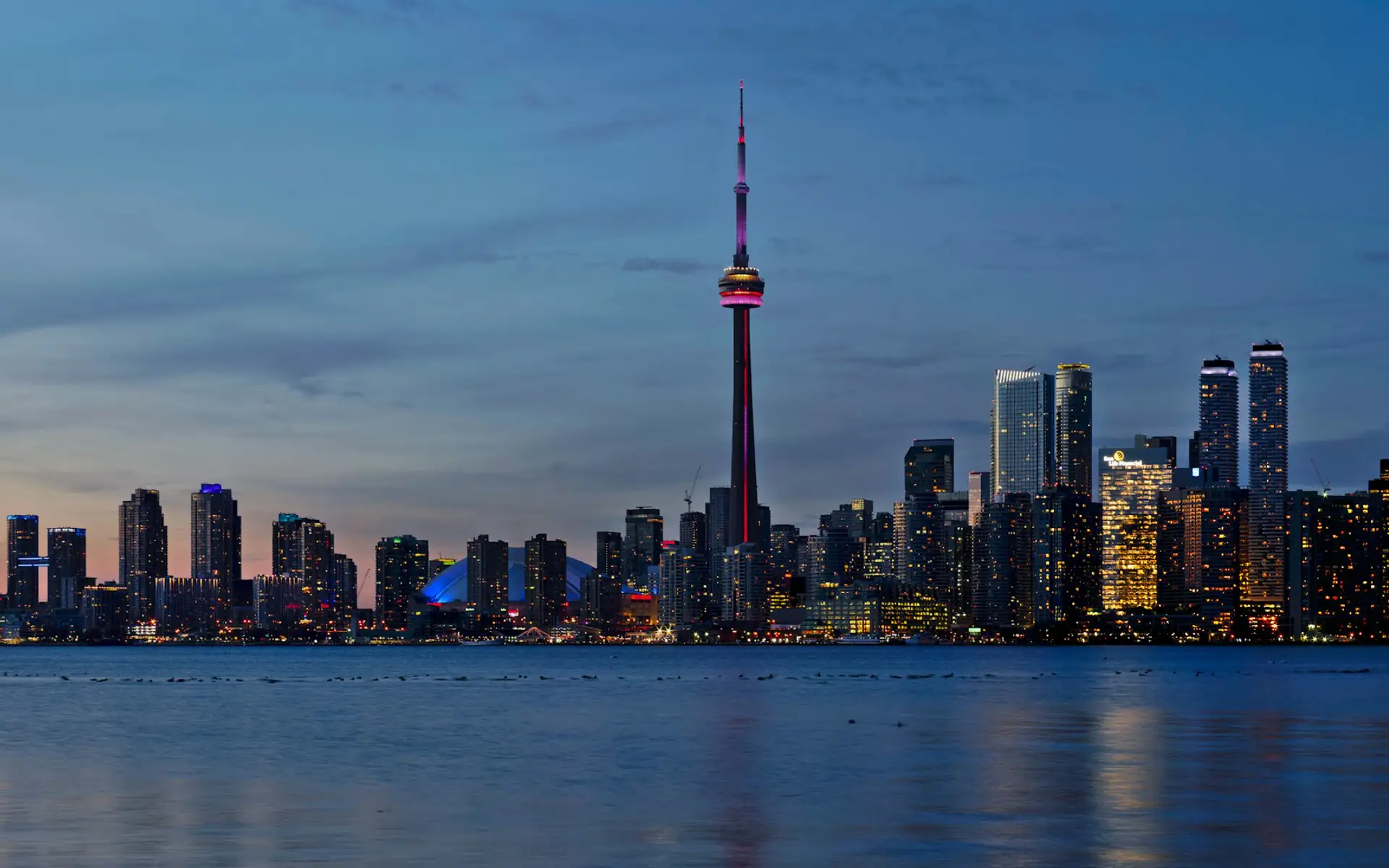 Toronto skyline and CN Tower lit up at dusk across the water