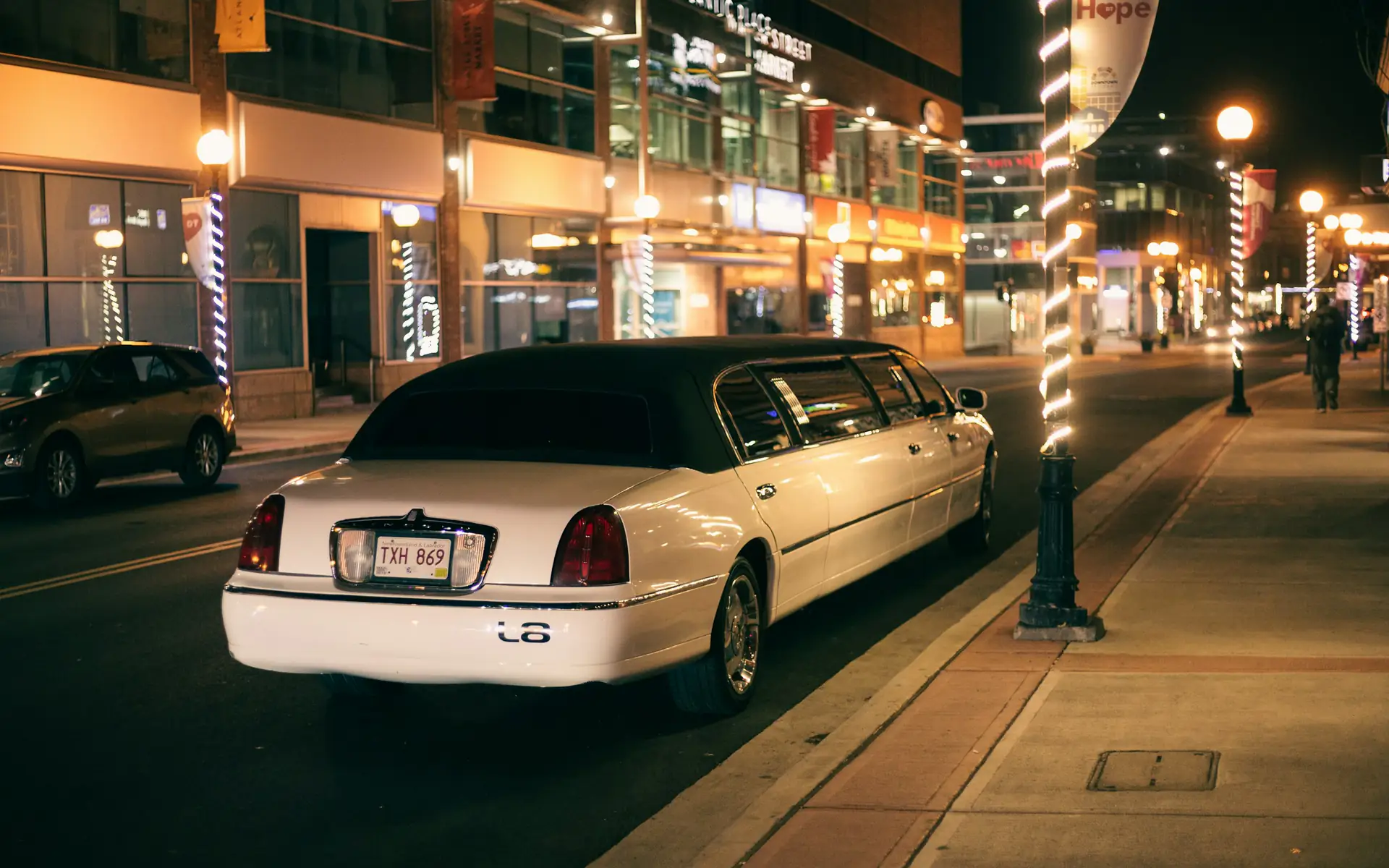 White stretch limousine parked on a lit downtown street at night
