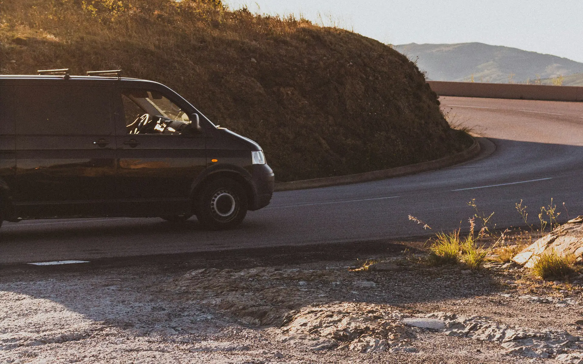 Black passenger van driving along a winding coastal road
