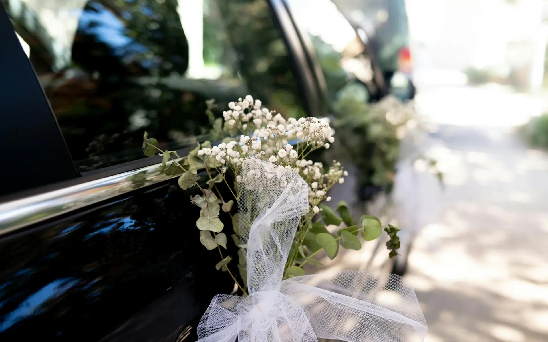 Bridal bouquet with white tulle tied to the door of a black car